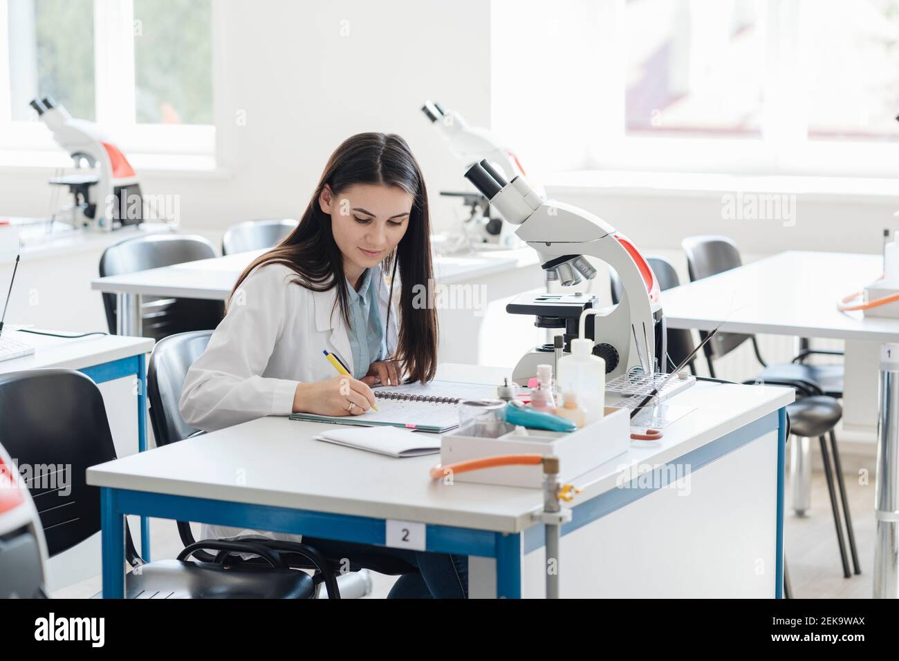 Jeune chercheur en manteau blanc prenant des notes en classe scientifique Banque D'Images