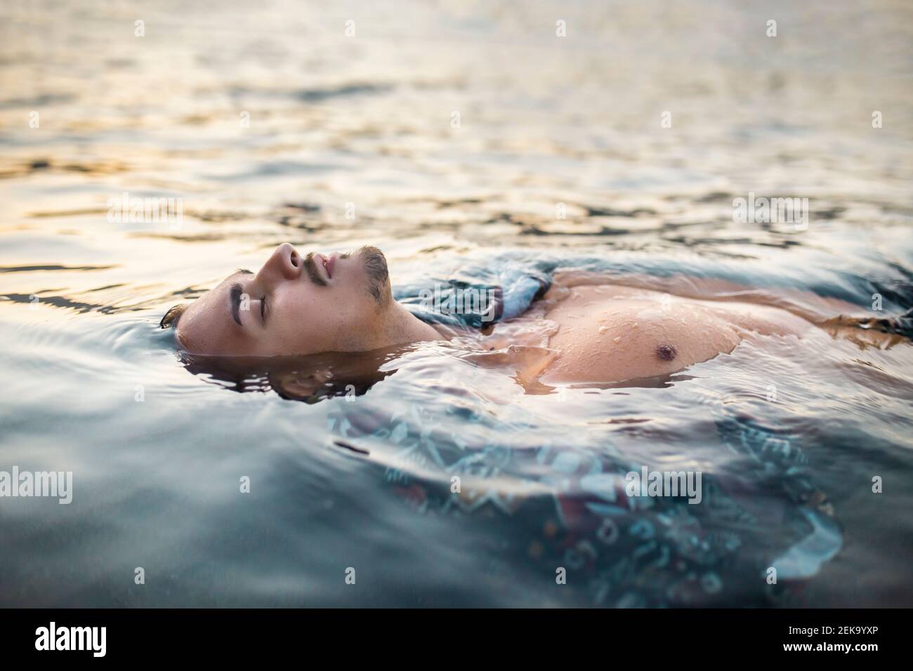 Jeune homme avec les yeux fermés flottant dans l'eau Banque D'Images