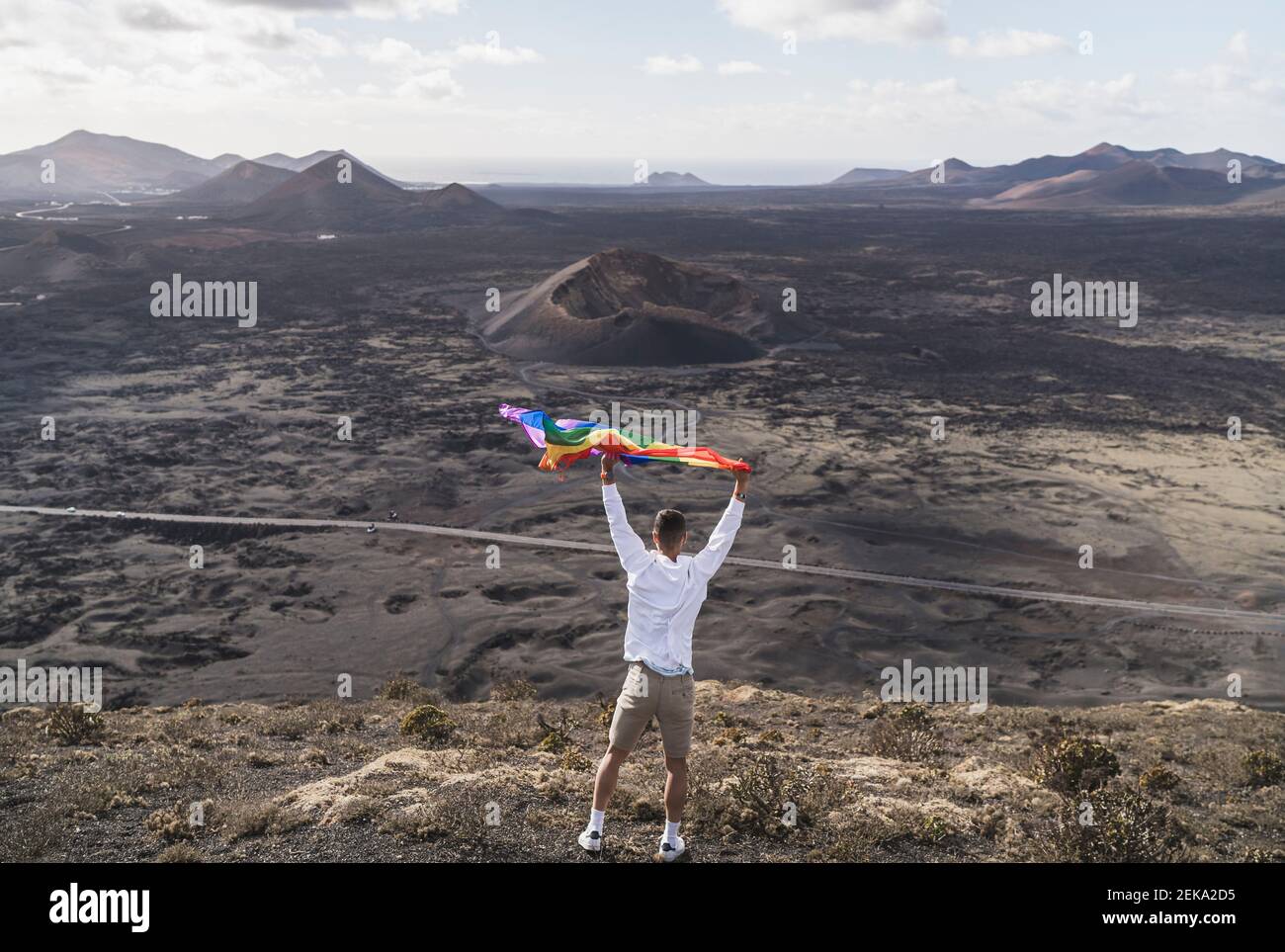 Un jeune touriste agite un arc-en-ciel en se tenant au volcan El Cuervo pendant ses vacances, Lanzarote, Espagne Banque D'Images