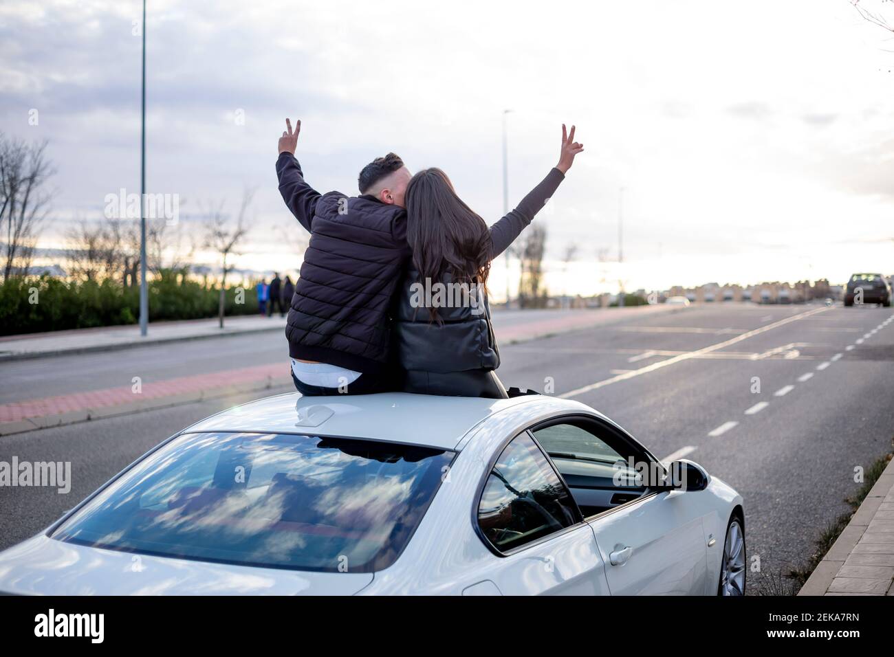 Couple sans souci signe de paix tout en étant assis n toit de voiture Banque D'Images