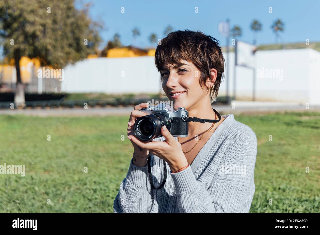 Femme souriante avec caméra analogique souriant pendant qu'elle est au parc Banque D'Images