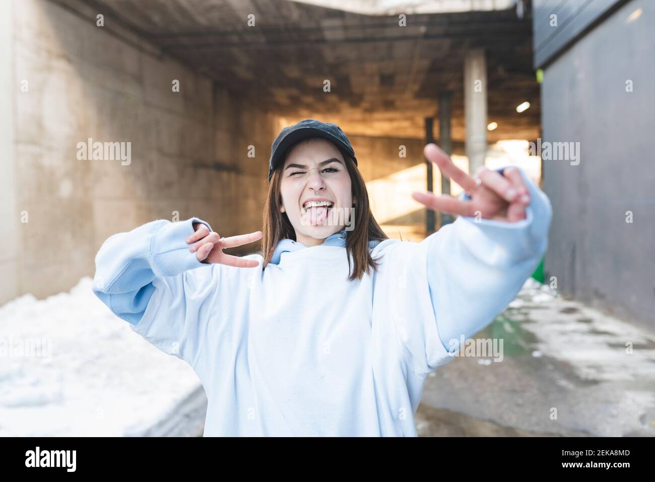 Jeune femme portant un chapeau gestant signe de paix tout en étant debout route en hiver Banque D'Images