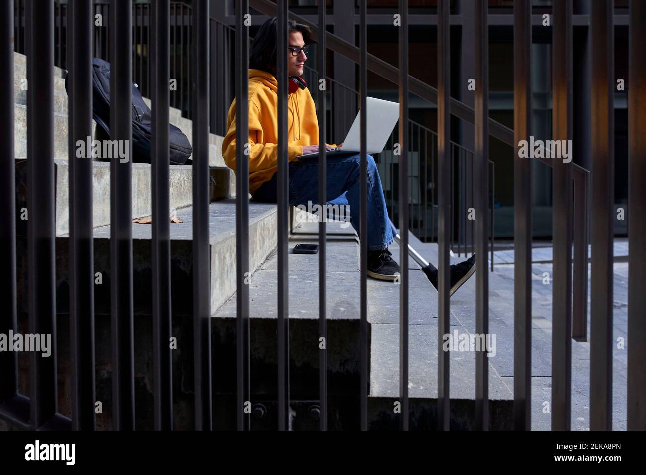 Homme handicapé avec prothèse de jambe utilisant un ordinateur portable tout en étant assis sur marches visibles à travers la main courante métallique Banque D'Images