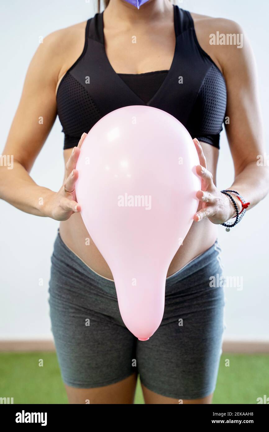 Femme enceinte tenant un ballon de couleur rose contre l'abdomen Banque D'Images
