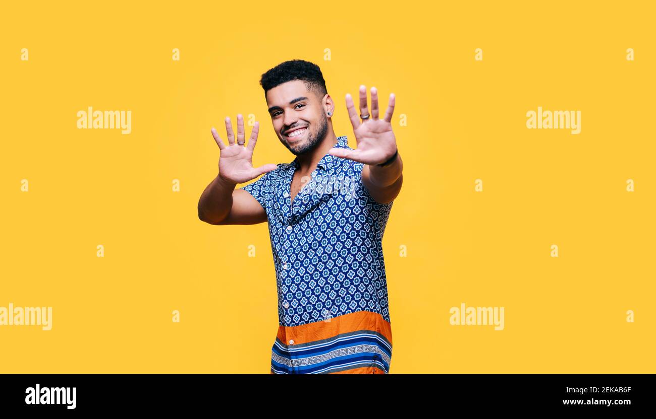 Homme souriant montrant un panneau d'arrêt sur fond jaune Banque D'Images