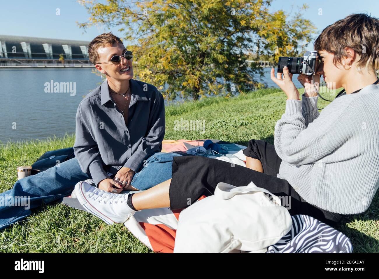 Jeune femme photographiant un ami souriant avec un appareil photo tout en étant assise stationnement Banque D'Images