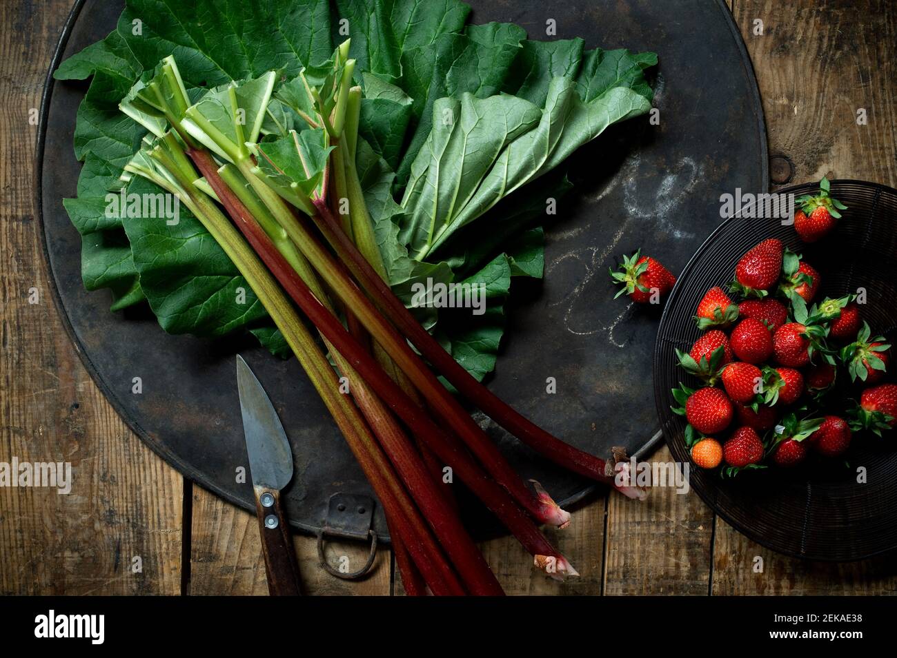 Couteau de cuisine, assiette de fraises et rhubarbe fraîche sur plaque de cuisson rustique Banque D'Images