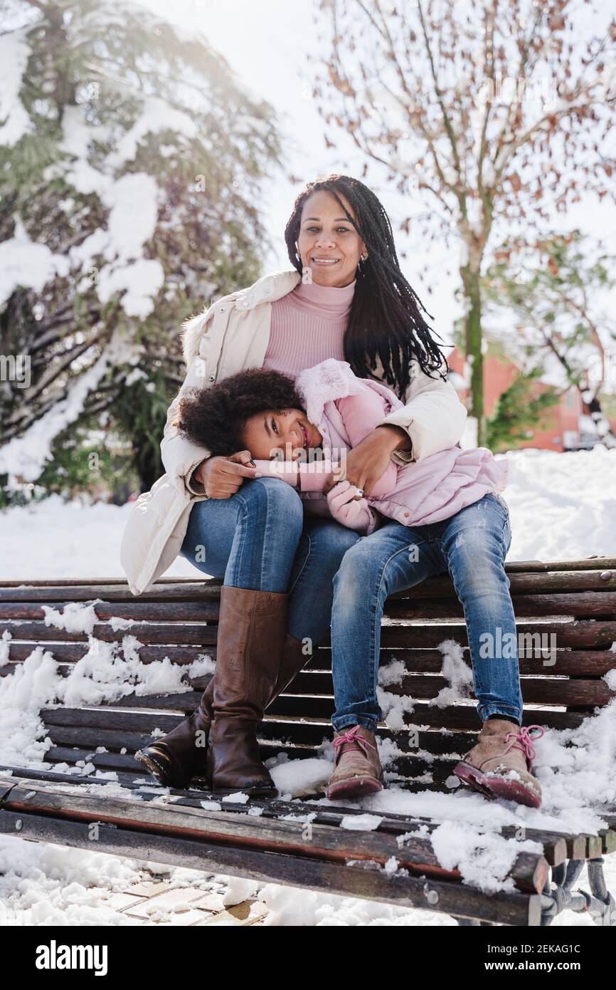 La fille repose la tête sur les genoux de sa mère tout en étant assise sur le banc dans le parc en hiver Banque D'Images