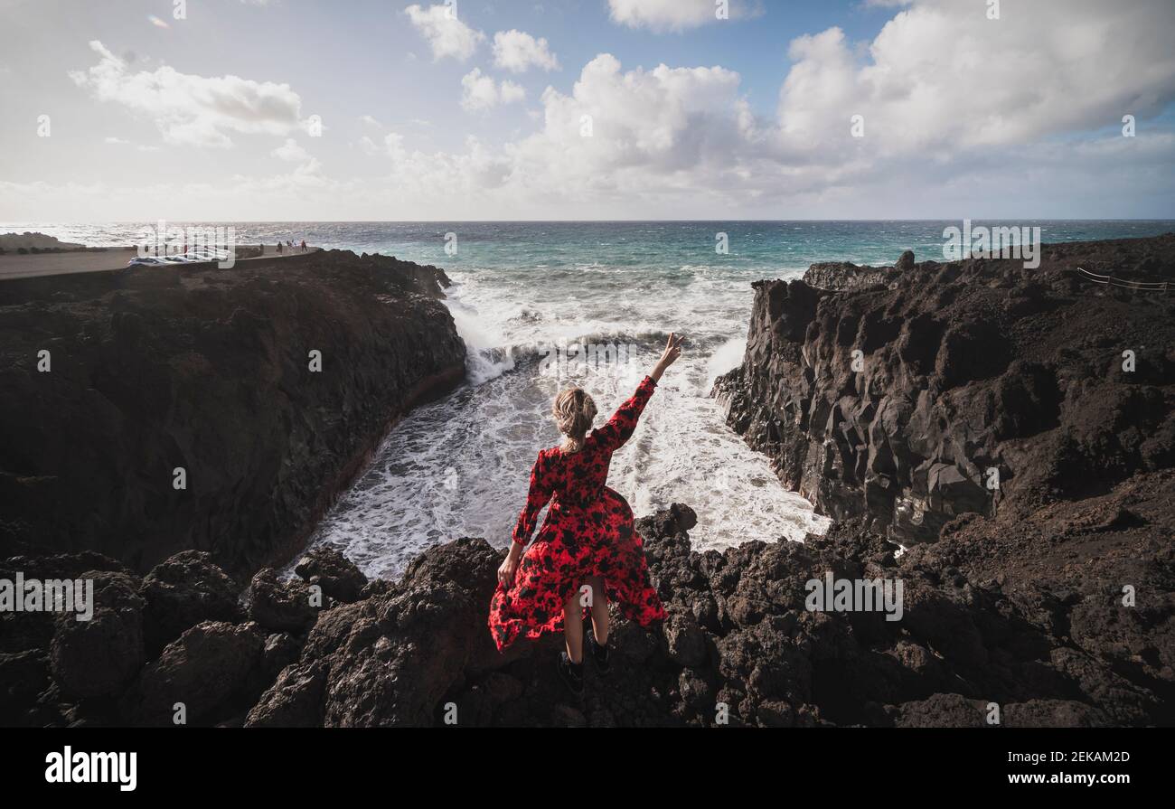 Jeune femme montrant le geste de la paix en se tenant sur la montagne à Los Hervideros, Lanzarote, Espagne Banque D'Images