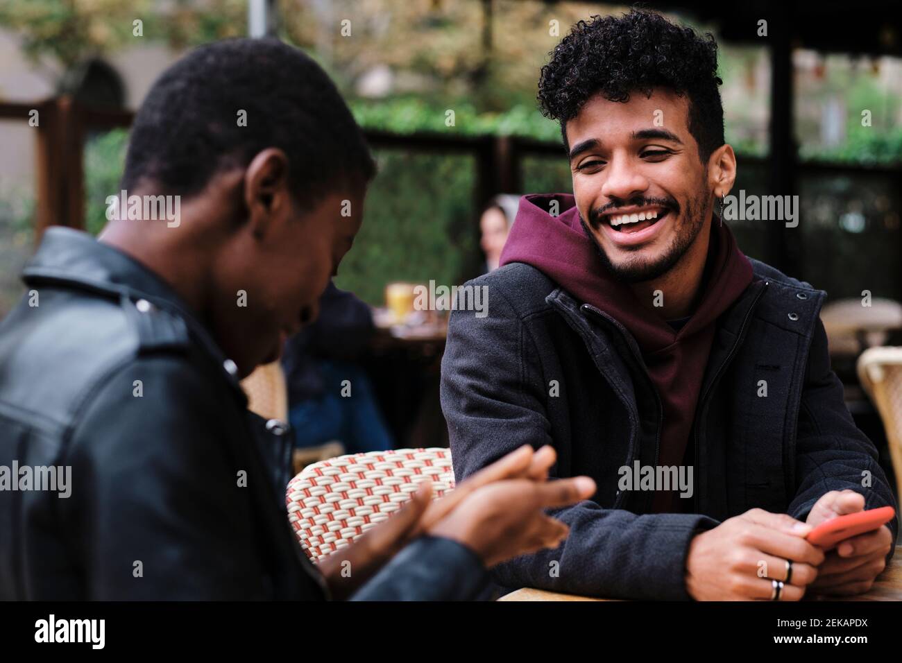 Homme souriant regardant un ami assis au café-terrasse Banque D'Images