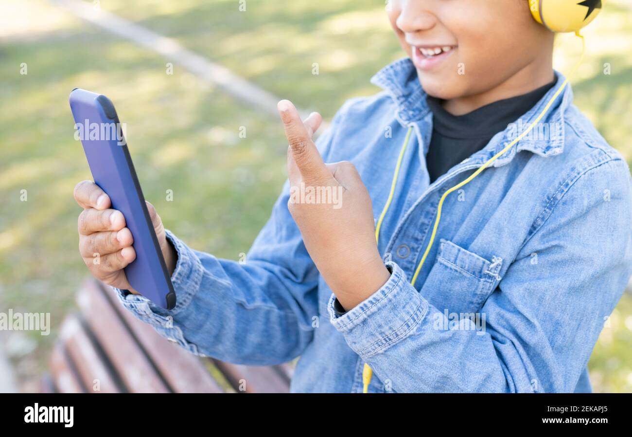Garçon montrant un geste de paix tout en utilisant un téléphone mobile au parc Banque D'Images