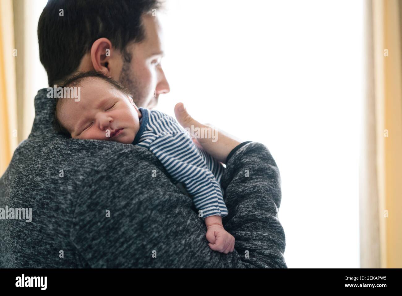 Père avec bébé garçon endormi regardant loin tout en se tenant debout fenêtre Banque D'Images