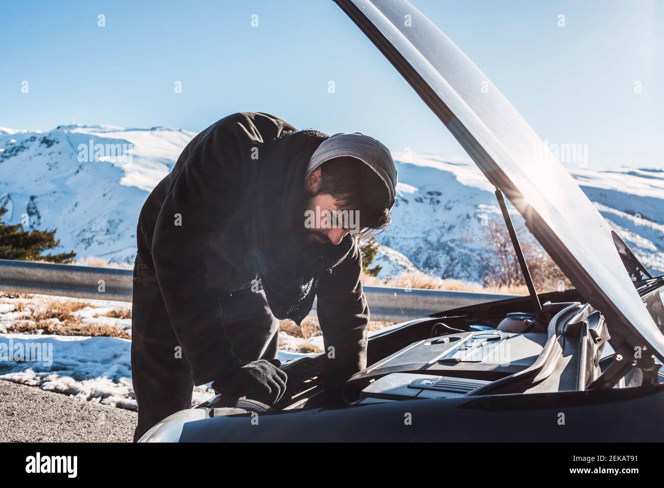 Homme répare la voiture sur un terrain couvert de neige contre le ciel pendant hiver Banque D'Images