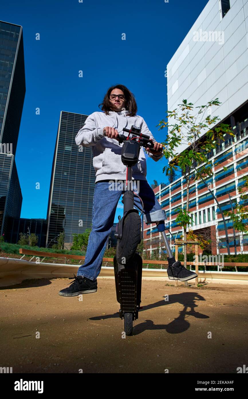 Jeune homme handicapé pratiquant le cascades sur un scooter électrique de poussée vers l'intérieur terrain de jeu contre les bâtiments de la ville Banque D'Images