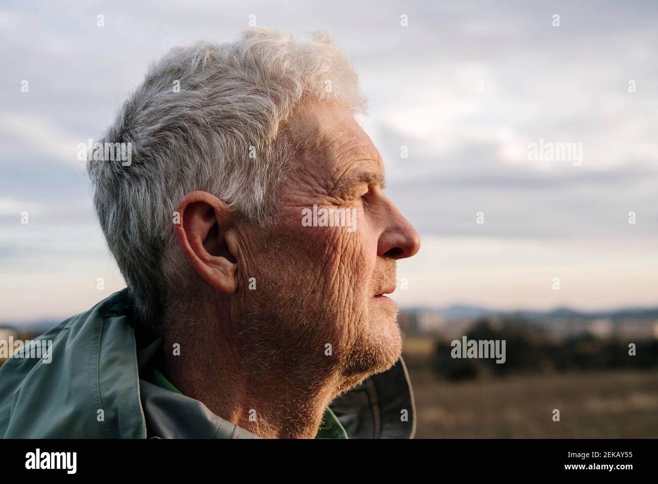Homme âgé avec le visage froissé contre ciel nuageux regardant loin Banque D'Images