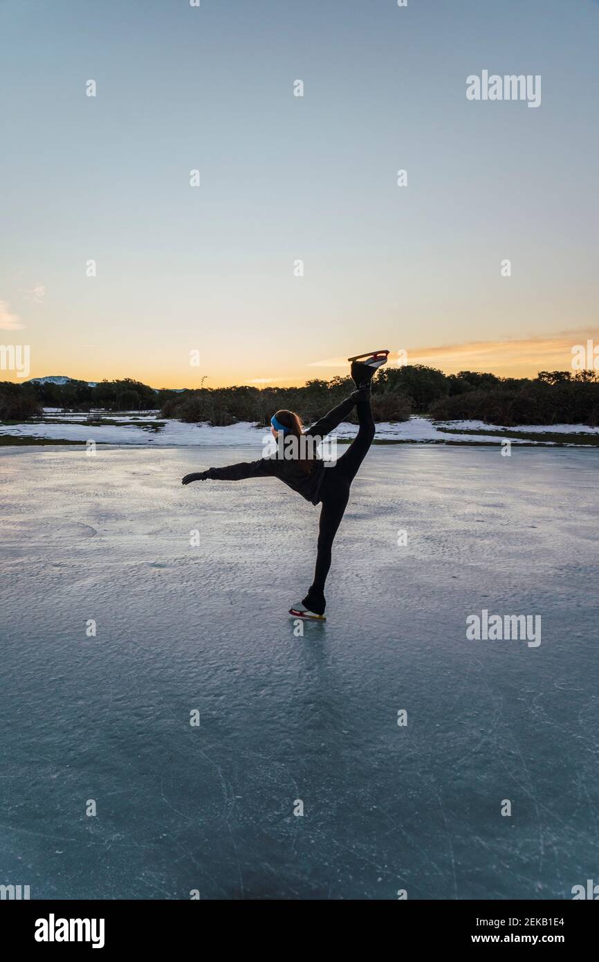 Patineuse féminine pratiquant sur un lac gelé au crépuscule Banque D'Images