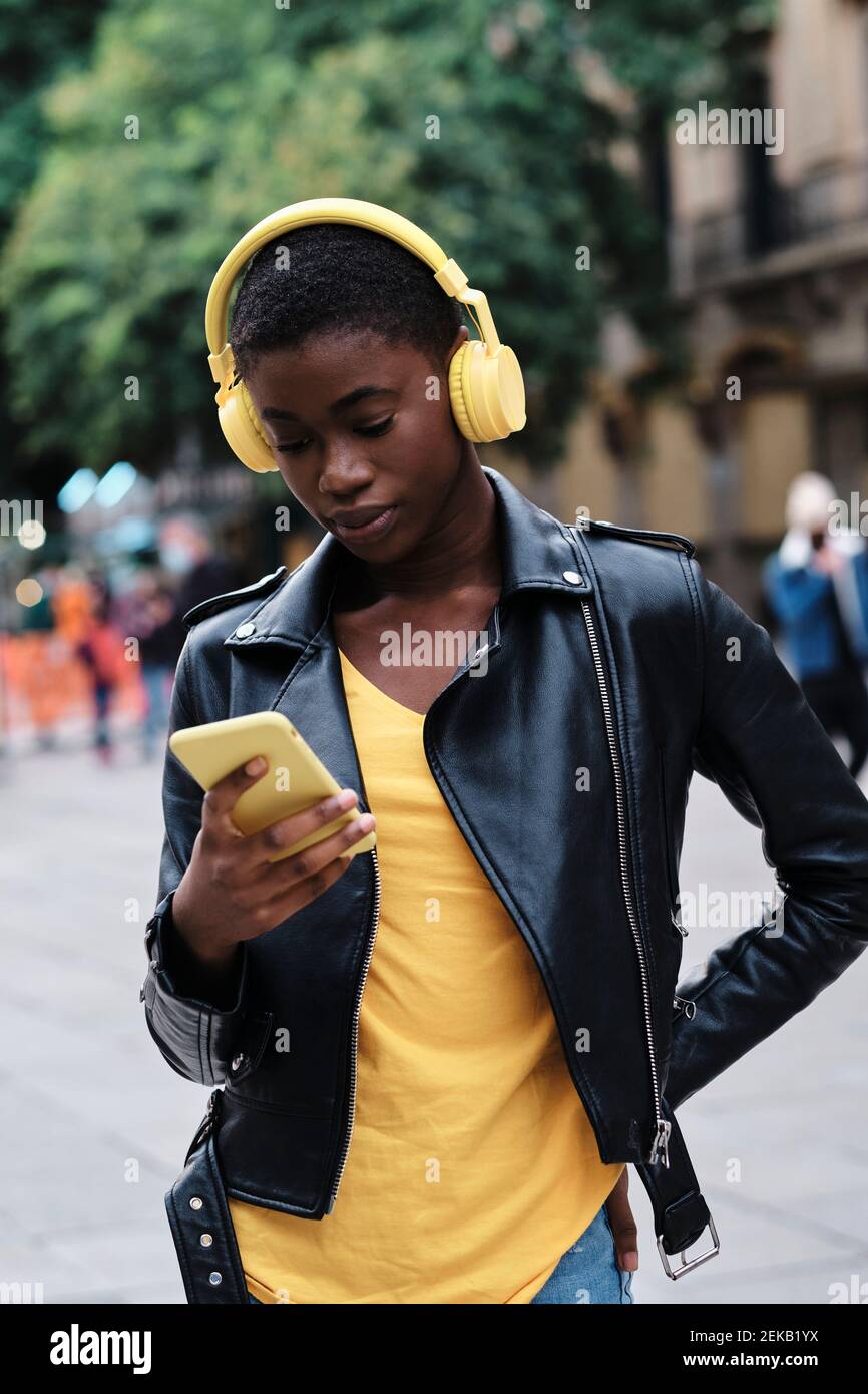 Une jeune femme porte un casque avec un smartphone tout en étant debout main sur la hanche en ville Banque D'Images
