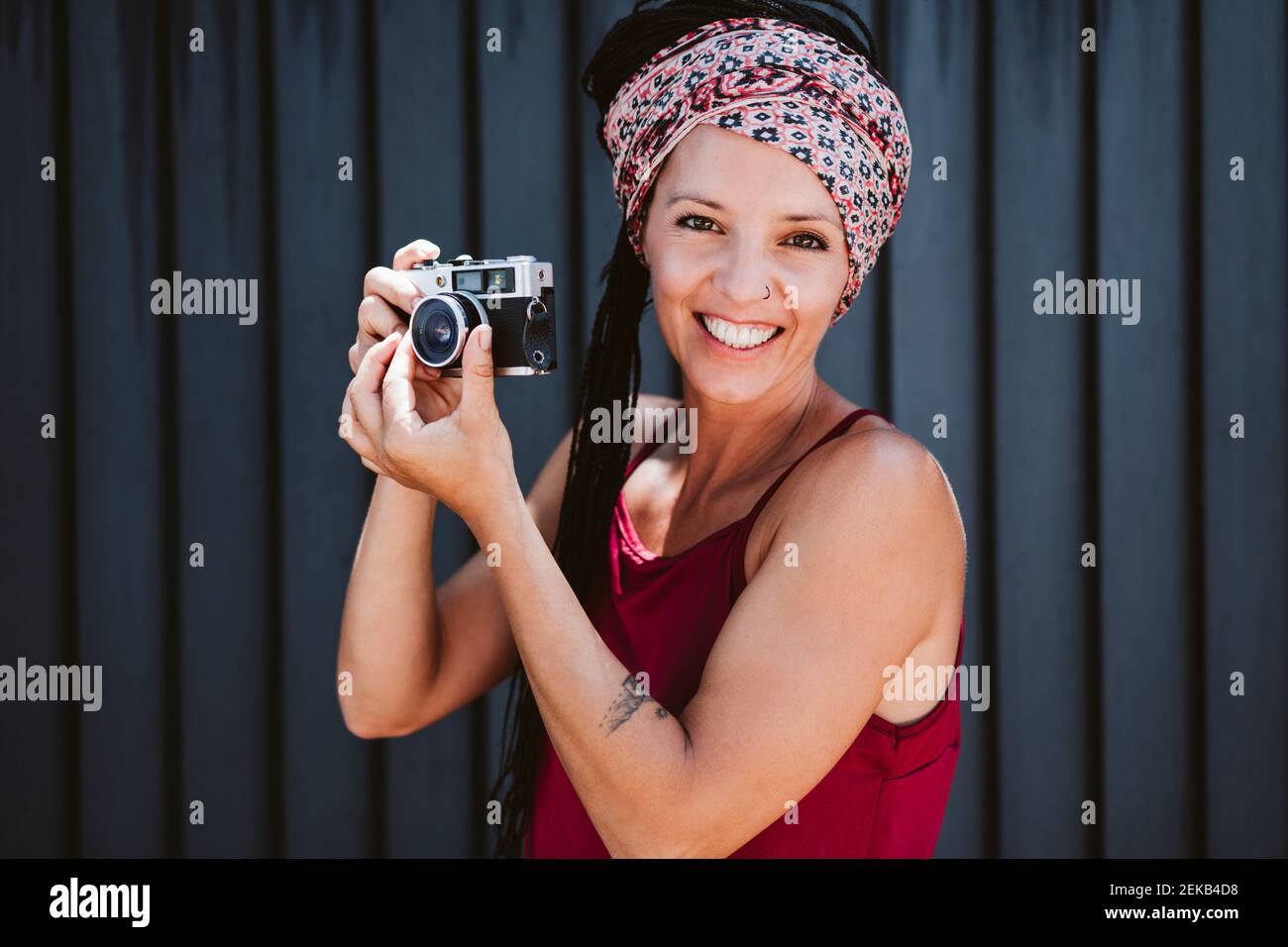 Femme souriante réglant l'objectif de l'appareil photo tout en se tenant contre le mur Banque D'Images