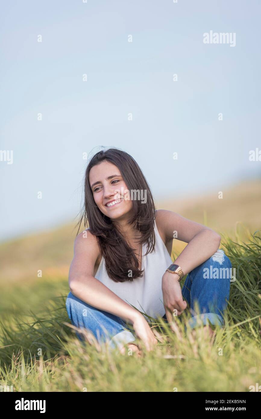 Une jeune femme heureuse qui regarde loin tout en étant assise sur l'herbe Banque D'Images