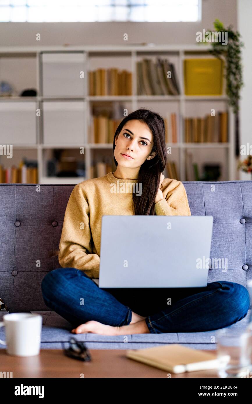 Jeune femme regardant tout en étant assise avec un ordinateur portable à la maison Banque D'Images