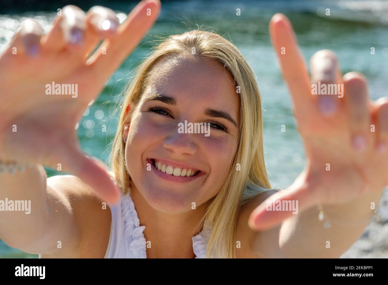 Jeune femme gaie montrant le cadre du doigt tout en se tenant contre le bord du lac le jour ensoleillé Banque D'Images