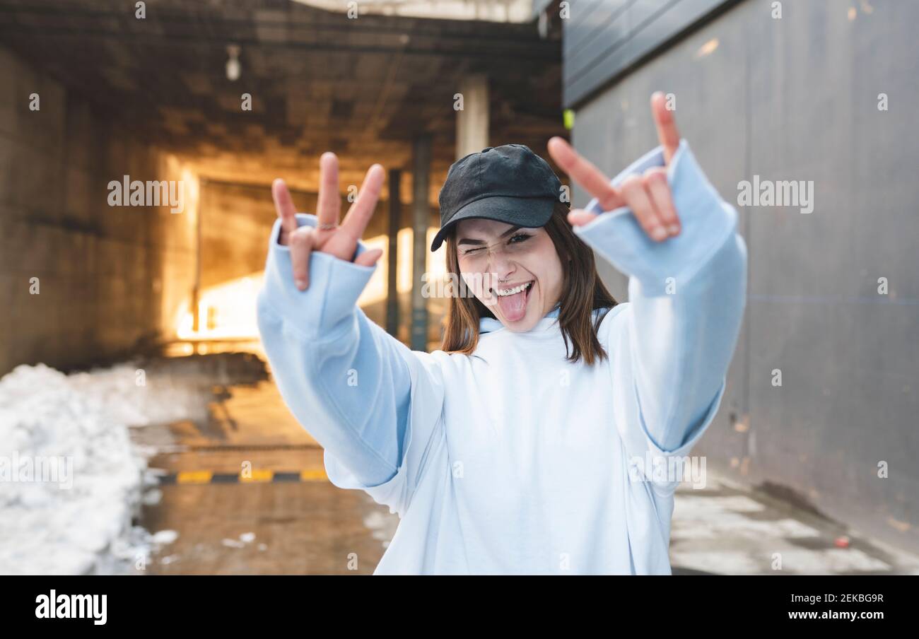 Femme portant une casquette montrant le geste de la corne en se tenant debout sur la route Banque D'Images