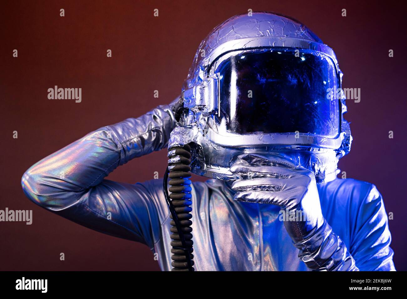 Un astronaute mâle tenant un casque d'espace tout en montrant le signe OK sur fond coloré Banque D'Images