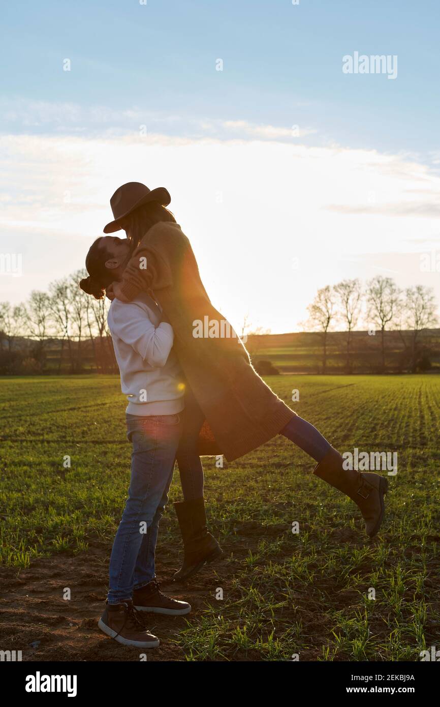 Homme levant une petite amie en se tenant sur une terre verte pendant le coucher du soleil Banque D'Images