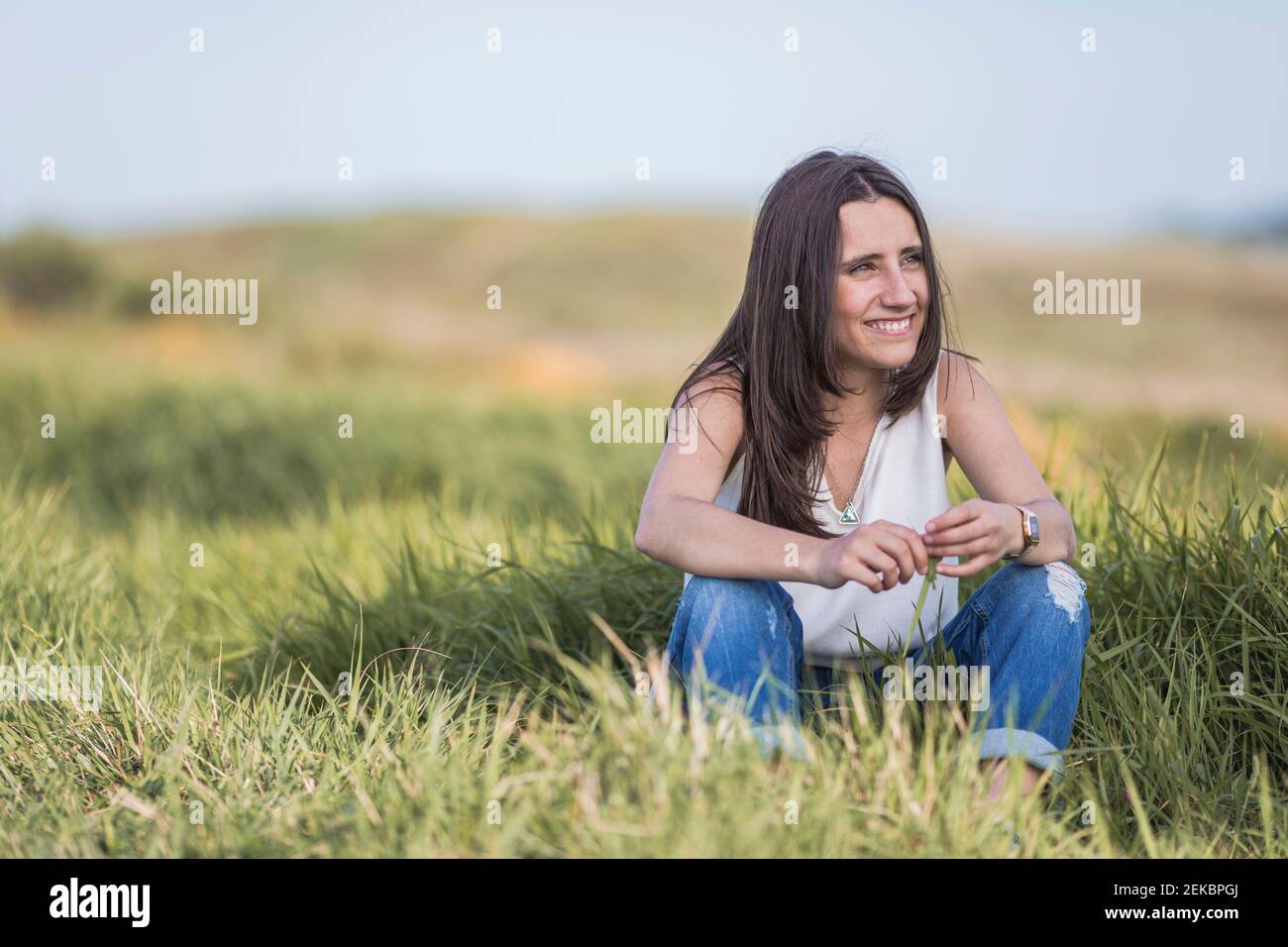 Belle jeune femme regardant loin en s'asseyant au milieu de l'herbe Banque D'Images
