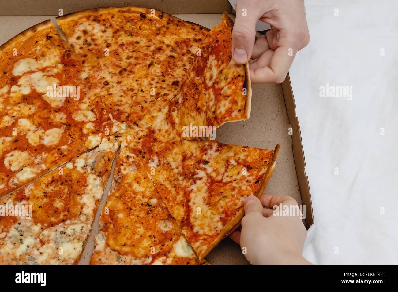 Deux mains prenant des tranches de pizza dans une boîte en carton Banque D'Images