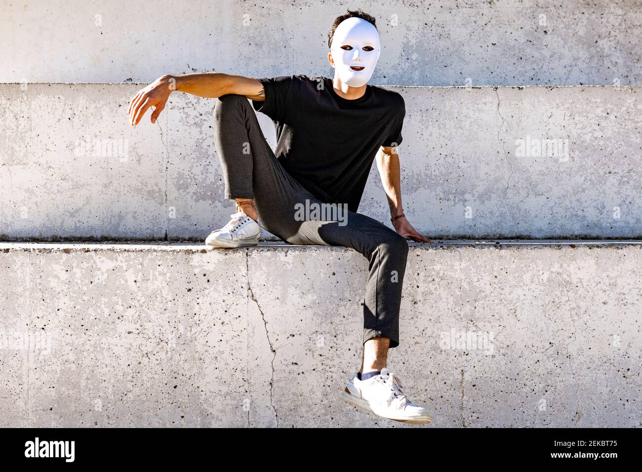Homme avec masque blanc assis sur le mur Banque D'Images