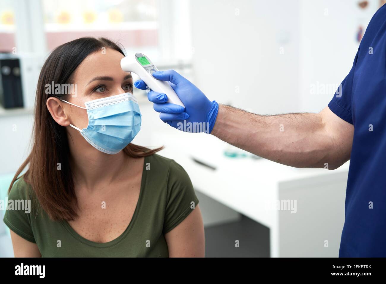 Médecin de sexe masculin utilisant un thermomètre infrarouge pour vérifier la température corporelle de la patiente Banque D'Images