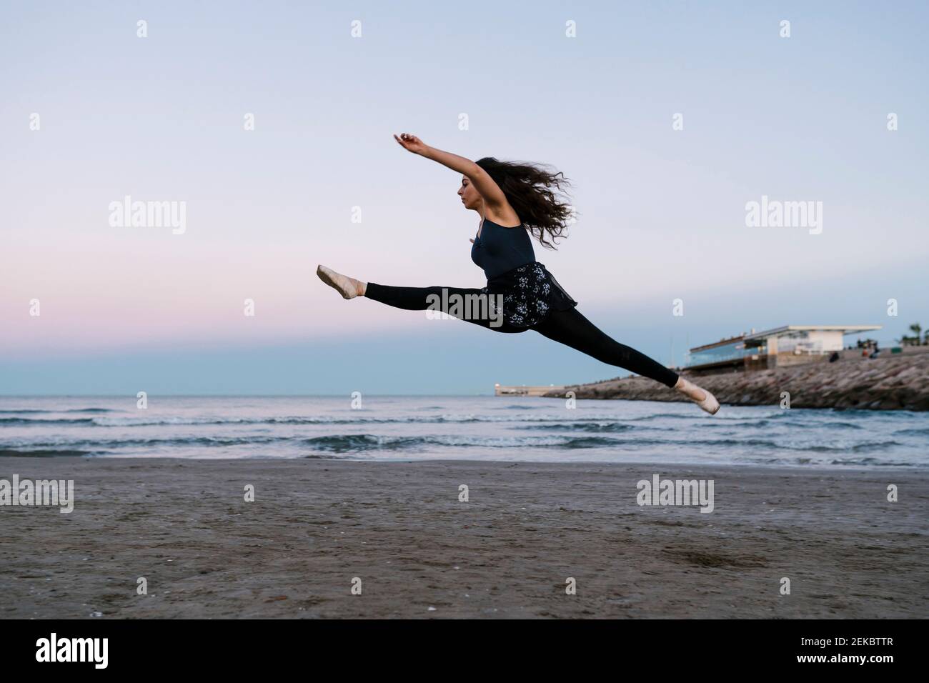 Danseuse de ballet féminine gracieuse, avec des jambes séparées, pratiquant à la plage au coucher du soleil Banque D'Images