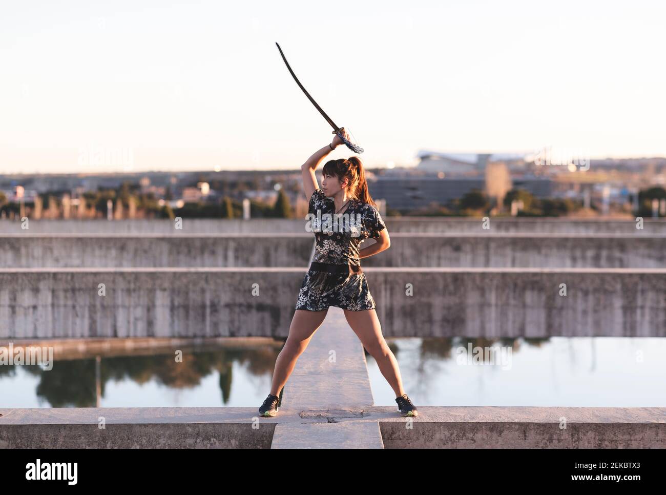 Jeune sportive pratiquant l'épée sur la structure contre le ciel clair au coucher du soleil Banque D'Images Jeune sportive pratiquant l'épée sur la structure contre le ciel clair au coucher du soleil Banque D'Images