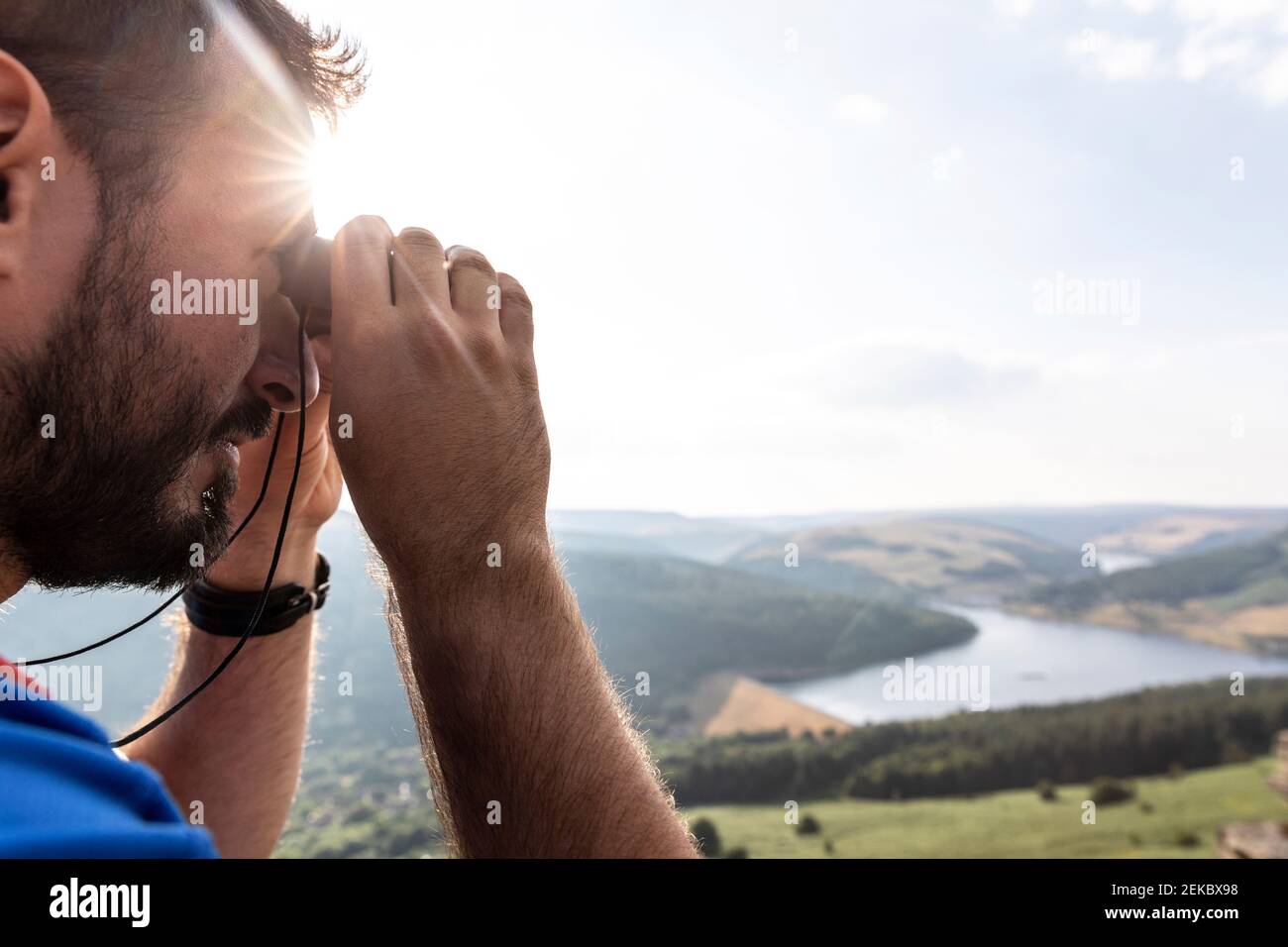 Jeune homme regardant la vue à travers des jumelles en plein soleil pendant vacances Banque D'Images