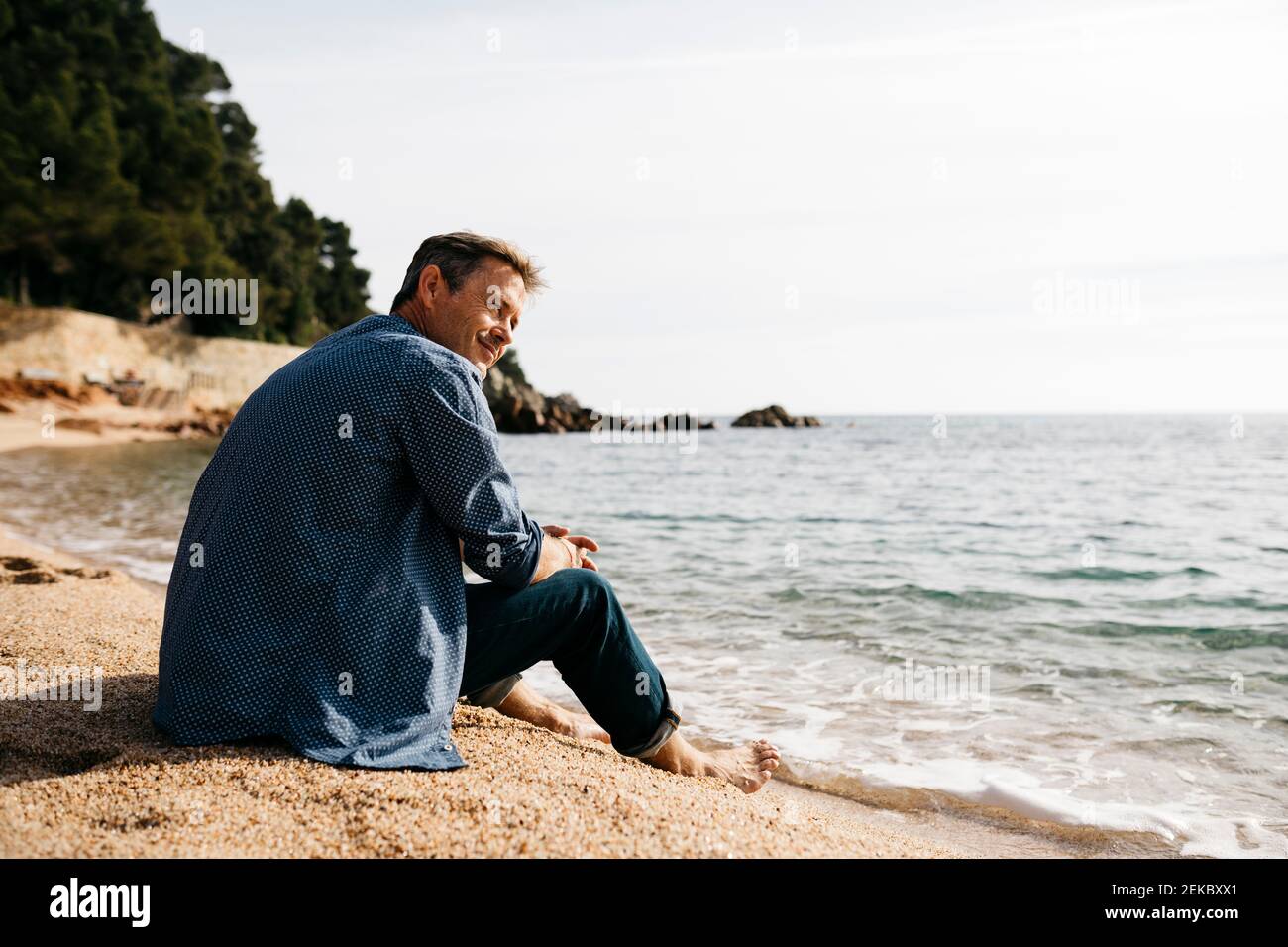 Homme souriant assis sur la plage tout en regardant loin contre la mer à la plage Banque D'Images
