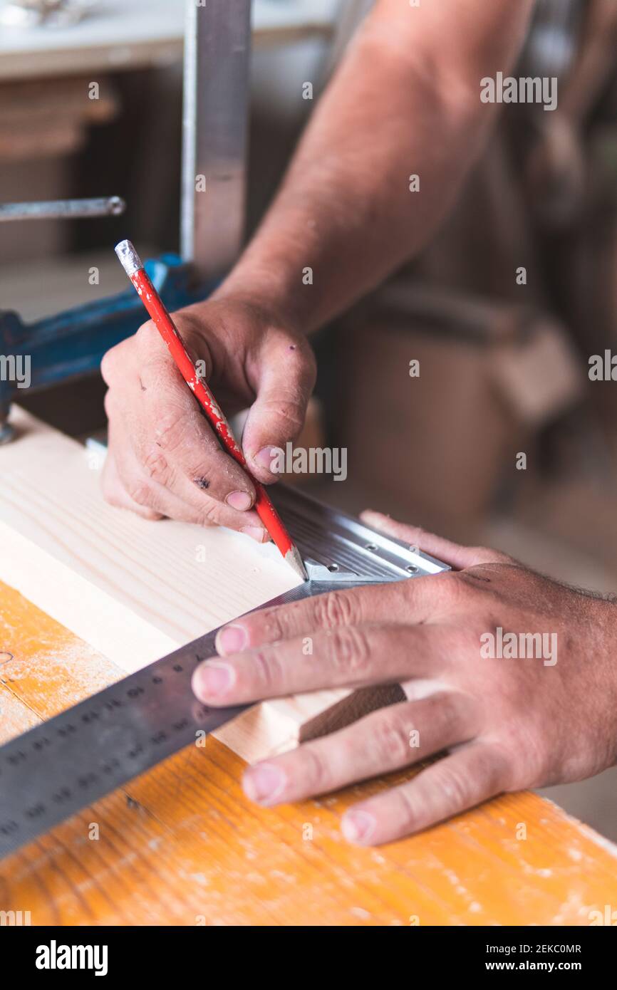 Marquage de menuisier jeune homme sur le bois à l'aide d'un crayon et d'une règle pendant le travail en atelier Banque D'Images