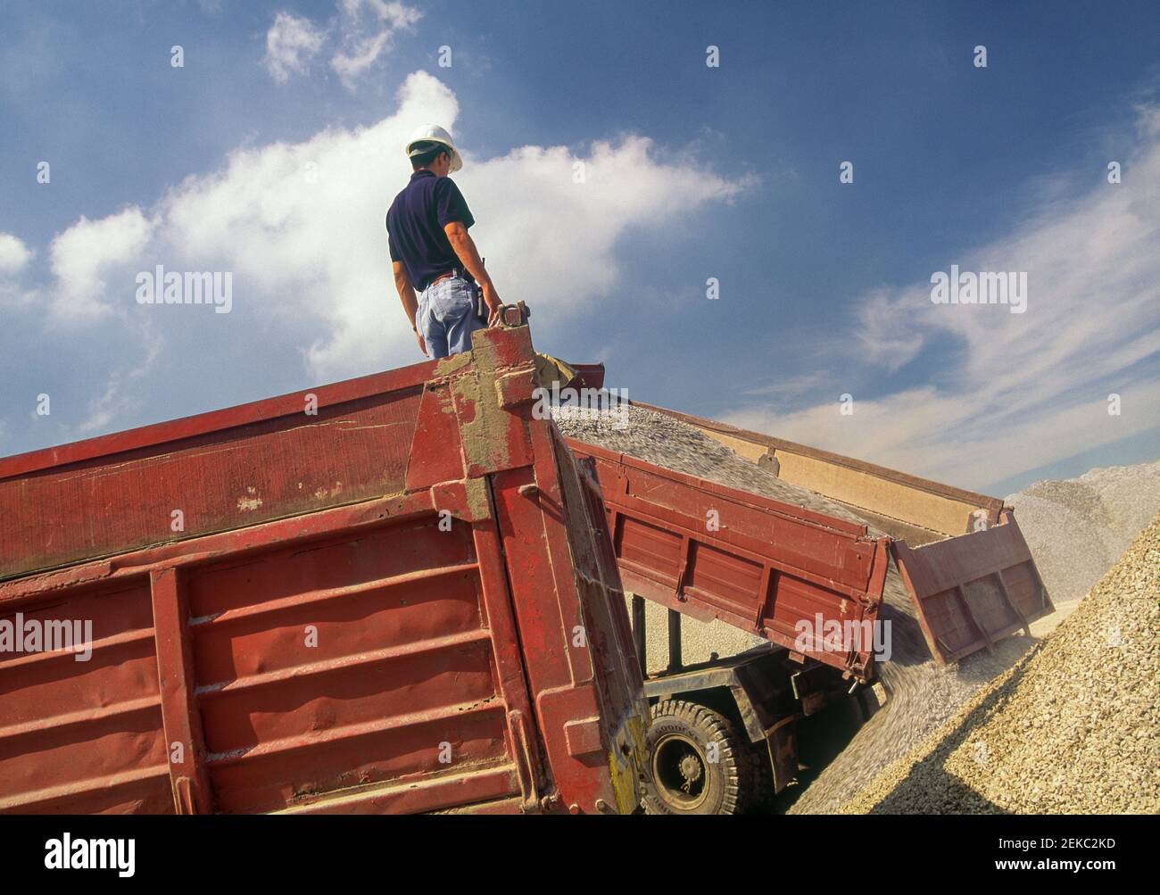 Travailleur debout sur camion-citerne, déchargeant le gravier sur le chantier. Banque D'Images