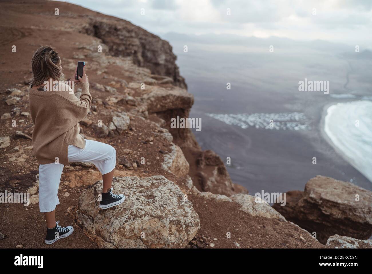 Une touriste féminine prend des photos par téléphone portable tout en se tenant sur la montagne à Famara Beach, Lanzarote, Espagne Banque D'Images