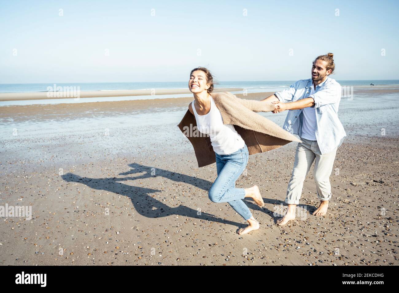 Jeune homme tenant les mains de sa petite amie tout en courant sur le sable à la plage Banque D'Images