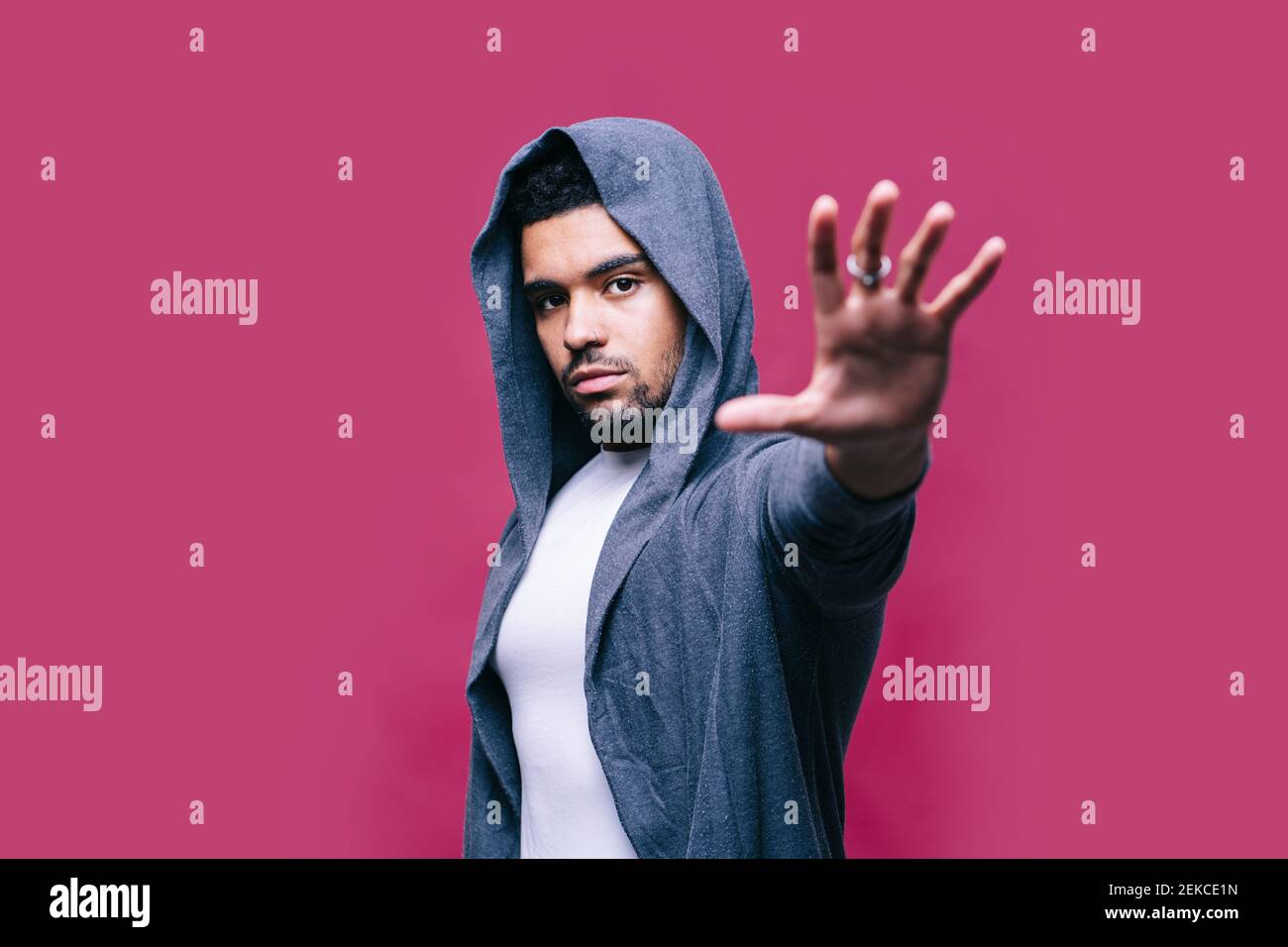 Homme en veste montrant un panneau d'arrêt sur fond rose Banque D'Images