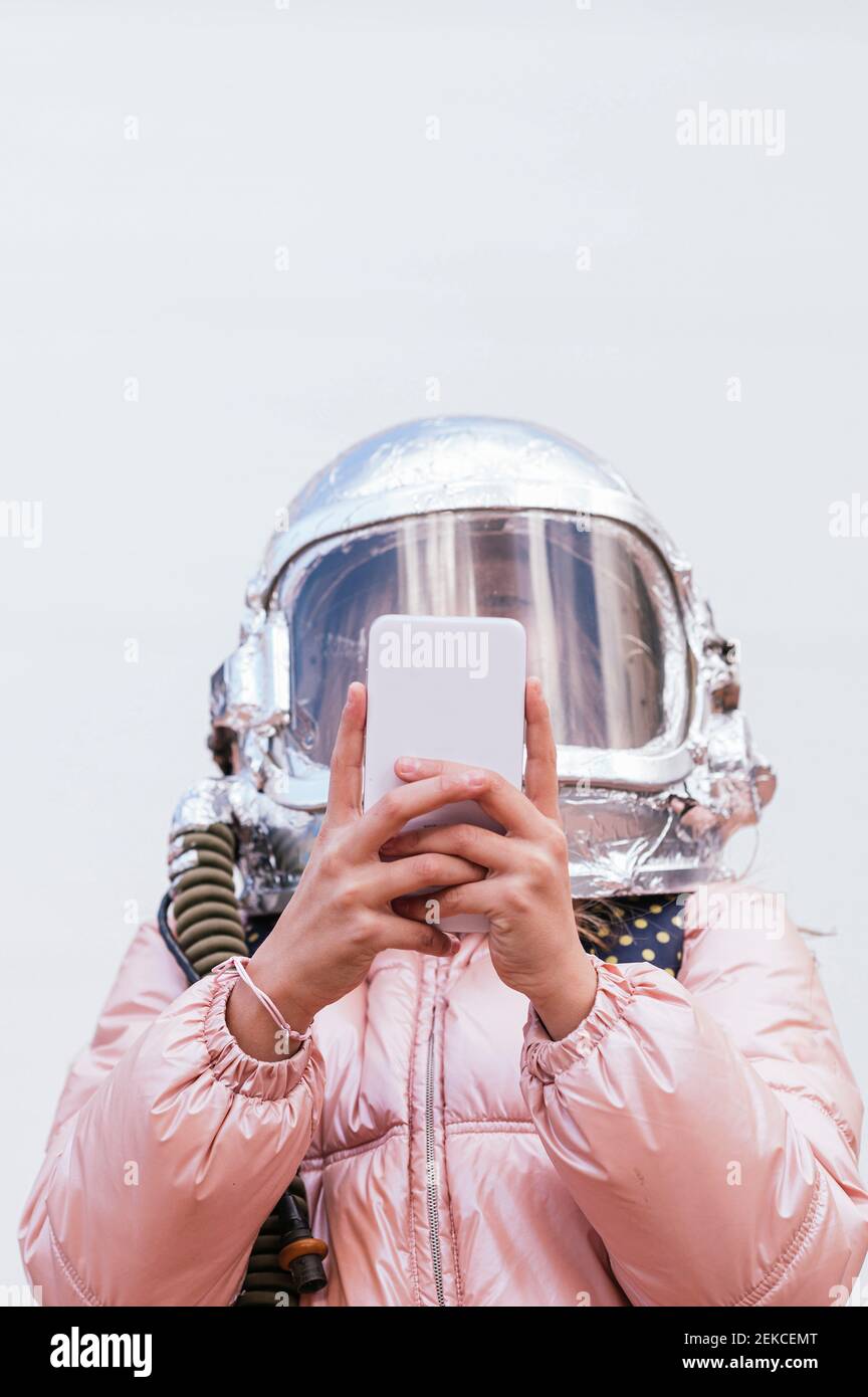 Fille avec un casque d'espace utilisant un téléphone mobile contre le mur Banque D'Images