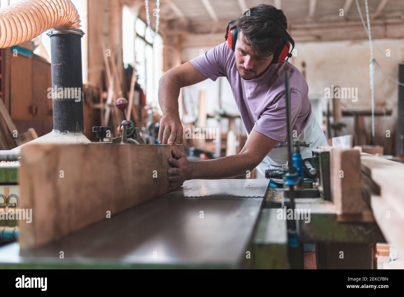 Jeune homme artisan tenant une planche en bois sur établi pendant le travail en atelier Banque D'Images