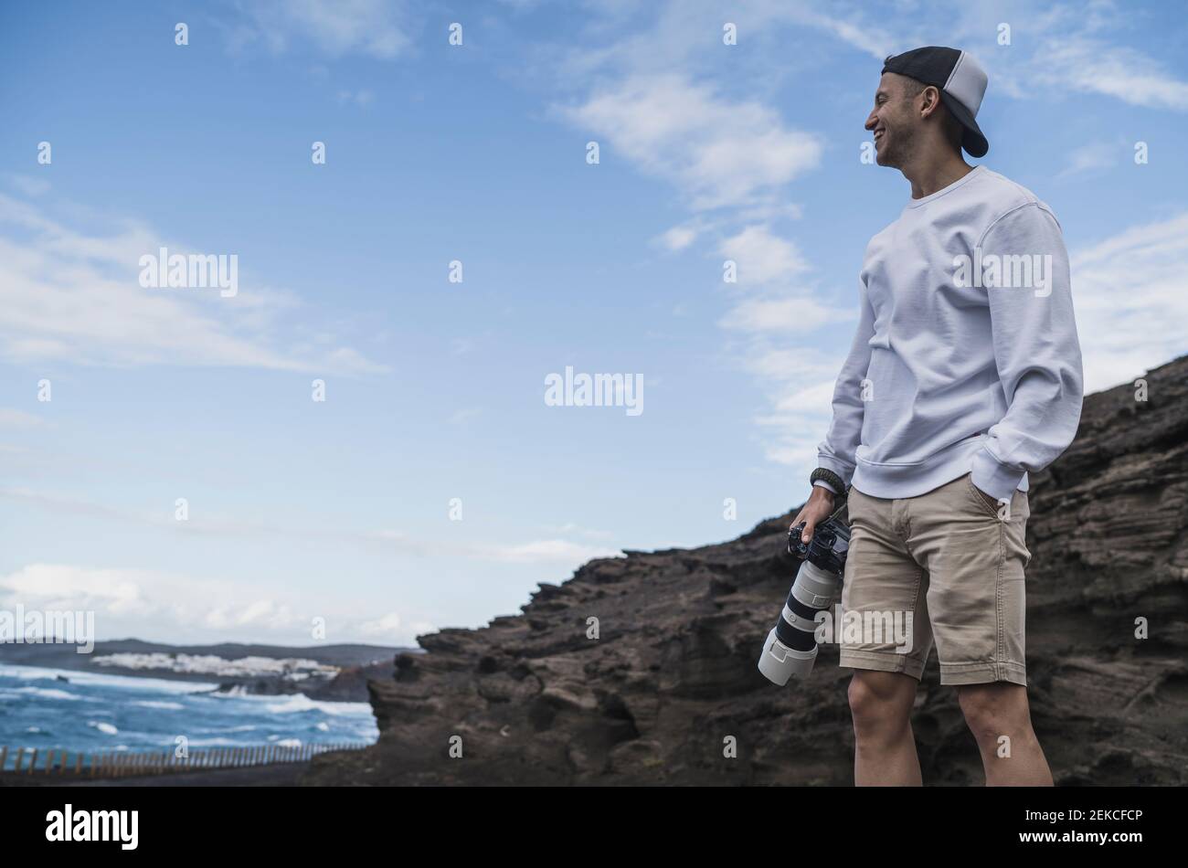 Souriant touriste mâle avec les mains dans les poches tenant l'appareil photo tout en regardant la vue à El golfo, Lanzarote, Espagne Banque D'Images