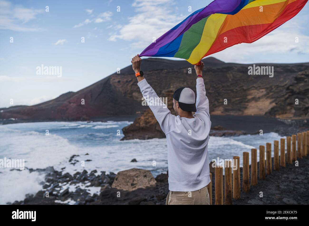 Un jeune touriste agite le drapeau arc-en-ciel tout en se tenant au point de vue El golfo, Lanzarote, Espagne Banque D'Images