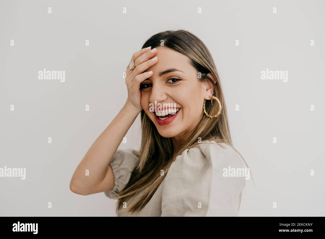 Belle femme avec la tête à la main tout en souriant contre le blanc arrière-plan Banque D'Images