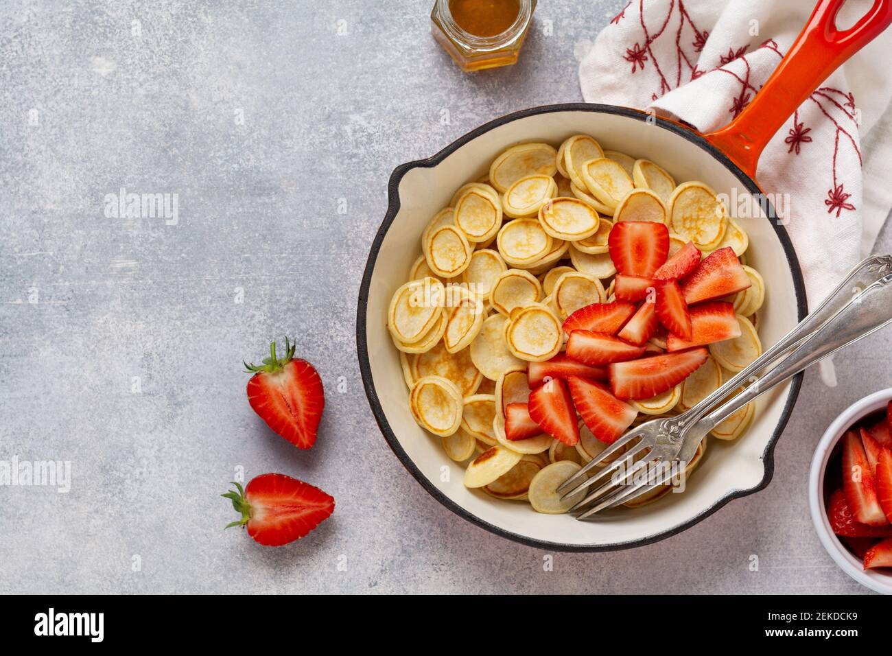 Mini céréales pancakes blanches avec fraises dans une poêle pour le petit déjeuner sur fond gris. Petit déjeuner à la mode avec de minuscules crêpes. Vue de dessus Banque D'Images