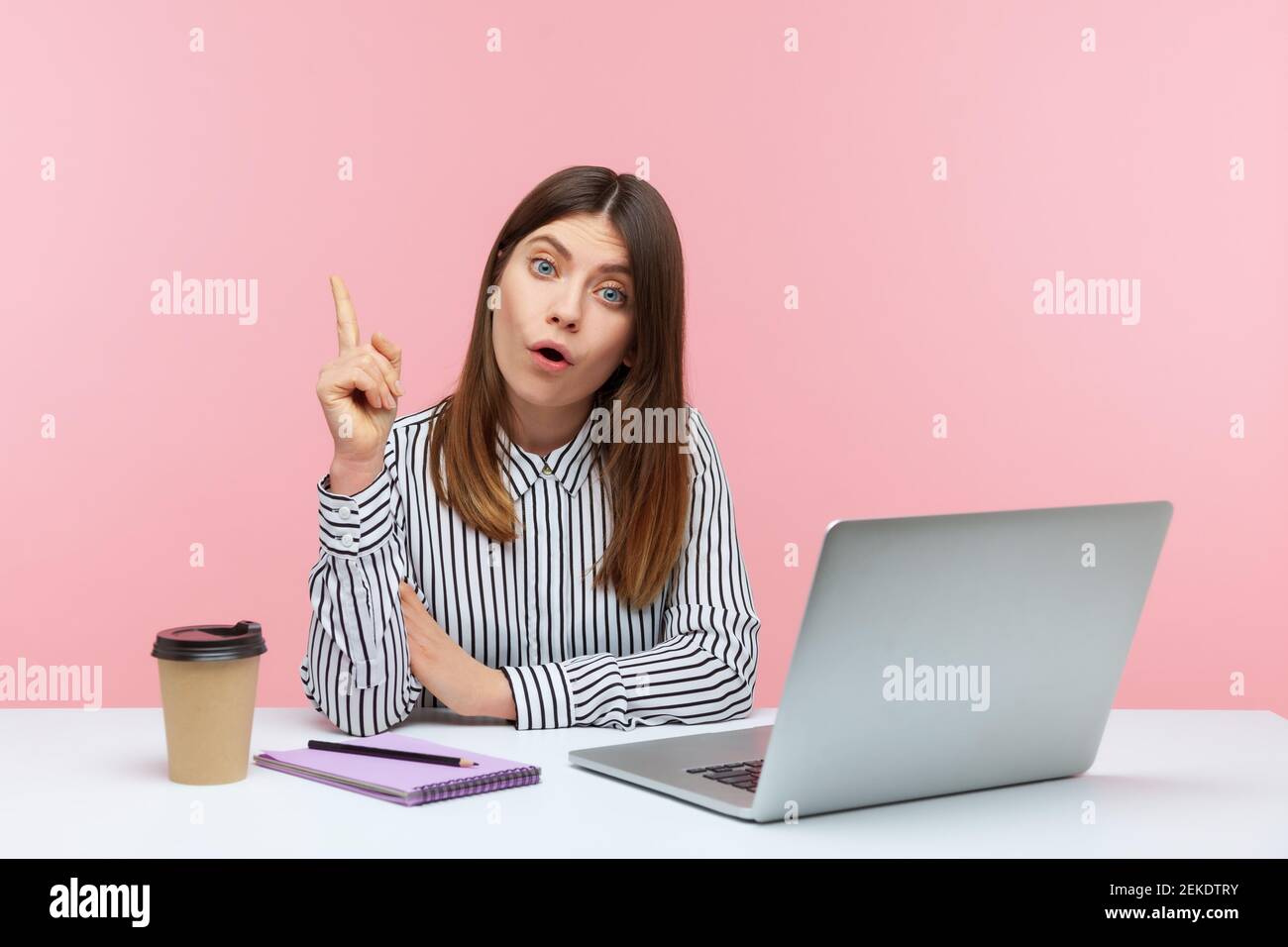 Solution d'entreprise ! Femme d'affaires excitée dans une chemise à rayures regardant surpris par l'idée de génie, levant le doigt vers le haut inspiré par la pensée créative de travail plac Banque D'Images