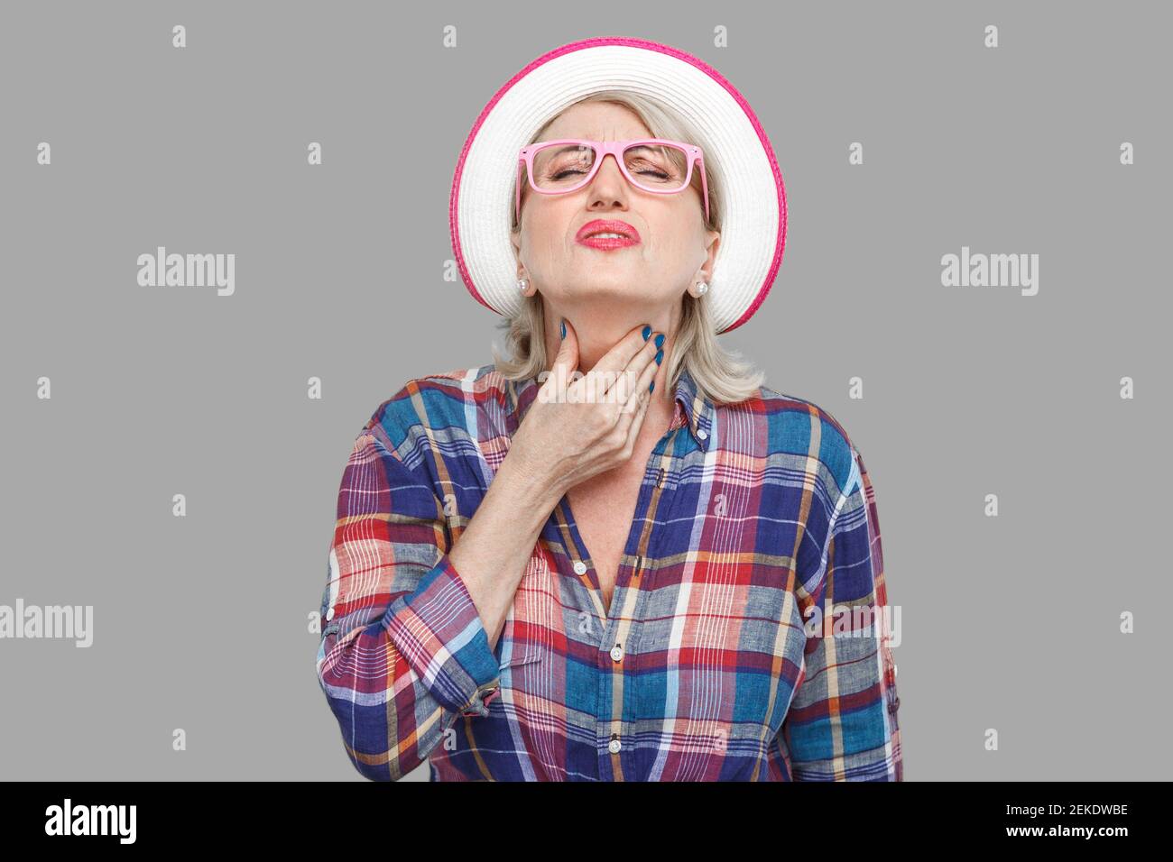 La maladie de gorge ou de la grippe. Portrait de femme mature élégant moderne malade dans un style décontracté avec chapeau et lunettes debout et tenant son cou douloureux Banque D'Images