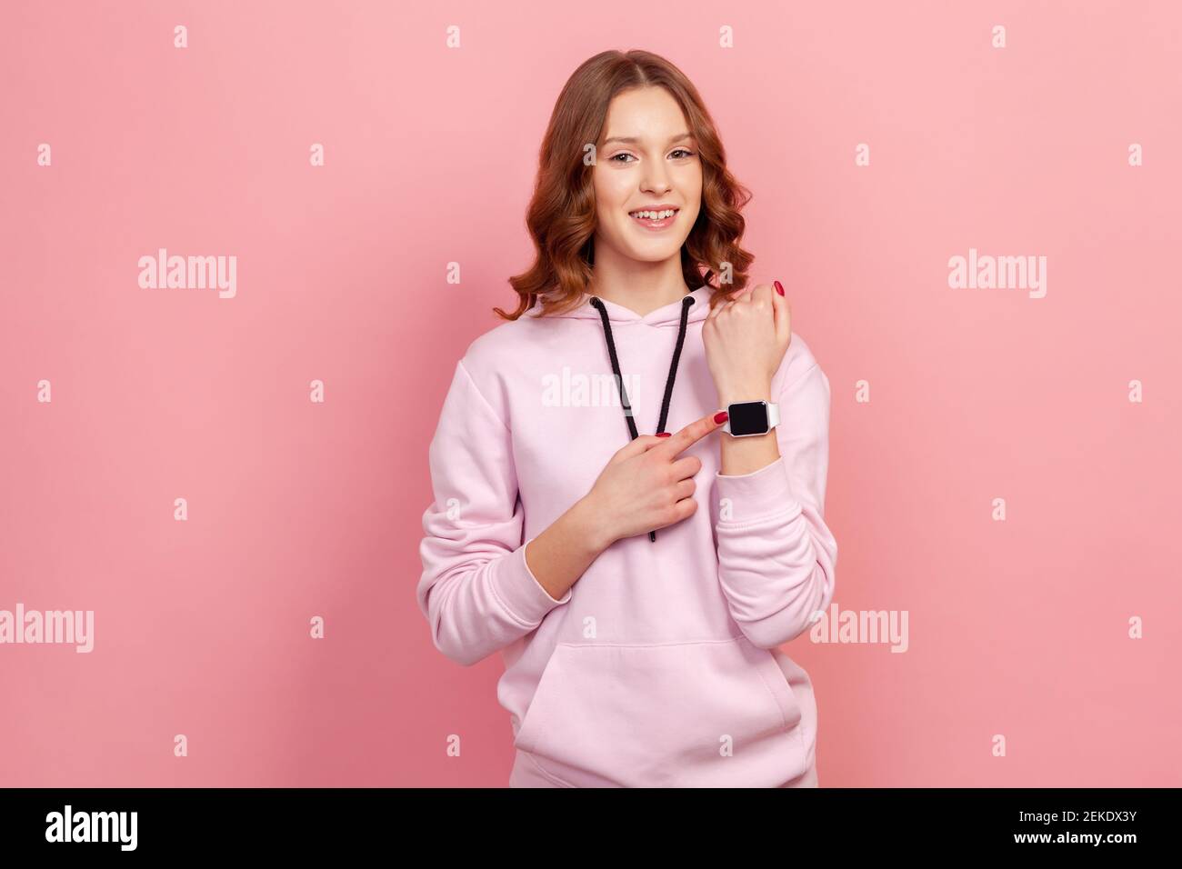 Portrait d'une jeune femme brune gaie en montre-bracelet pointée à capuche et souriante, montrant l'heure de la réunion convenue, des minutes heureuses. Prise de vue en studio en intérieur Banque D'Images